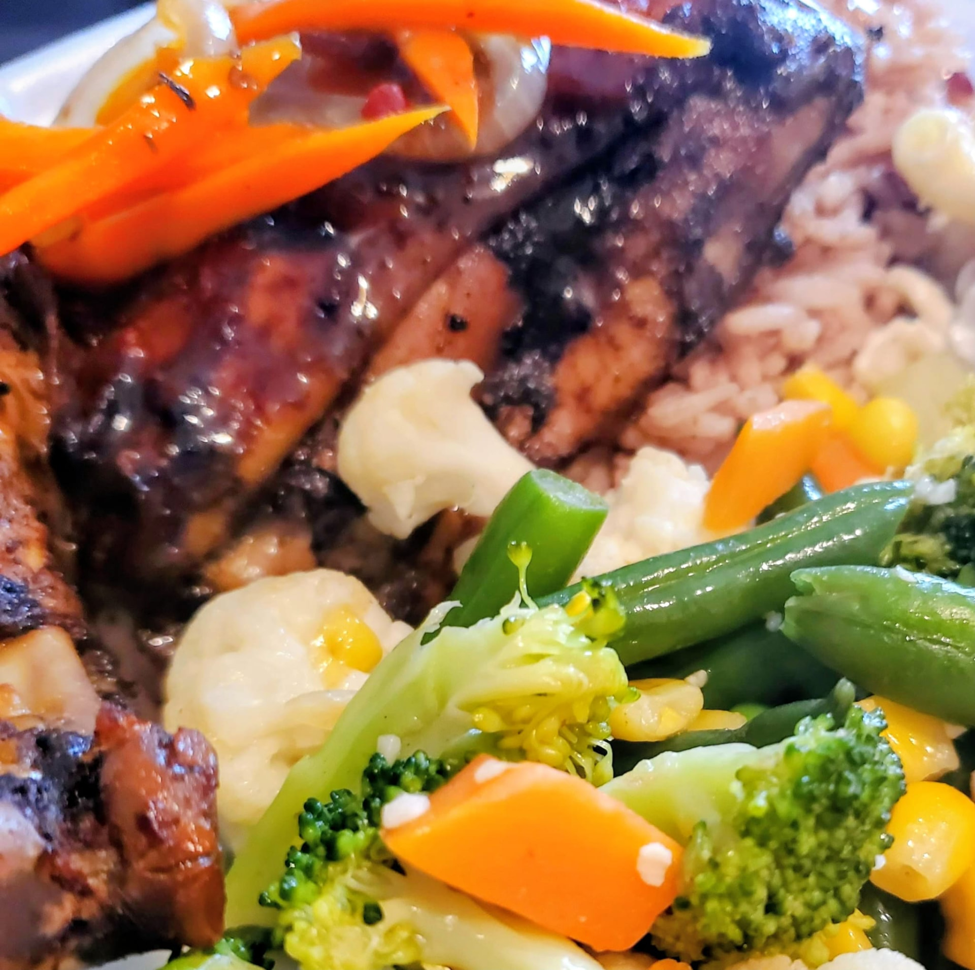 A plated jerk chicken dinner with rice and peas and fresh vegetables